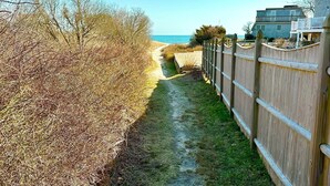 Een smal pad dat naar een strand leidt, afgegrensd door een houten omheining en droge begroeiing.