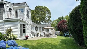 Een tweelaags huis met een overdekt terras, een gazon en diverse planten.