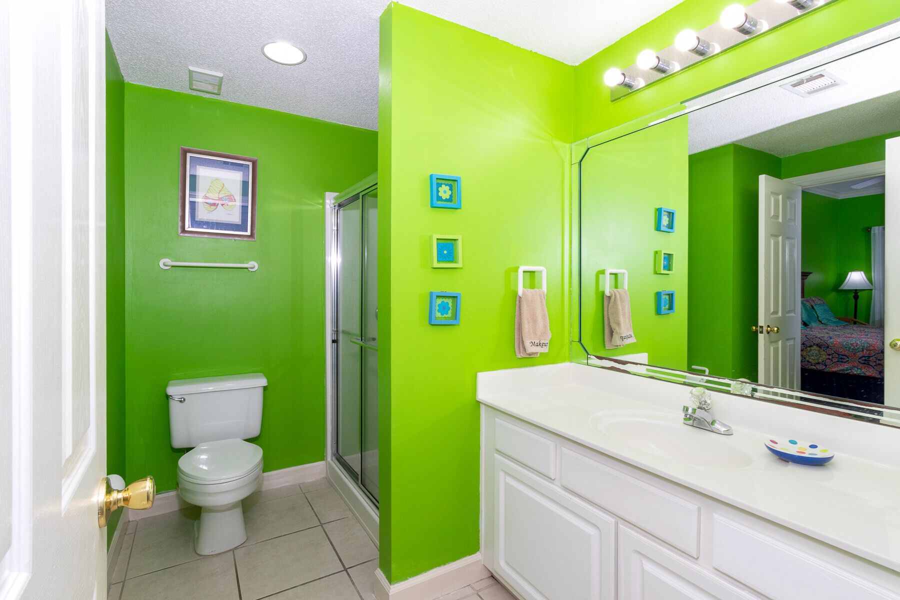 Une salle de bain avec des murs verts, des toilettes blanches, une douche en verre et un meuble-lavabo blanc avec un miroir.
