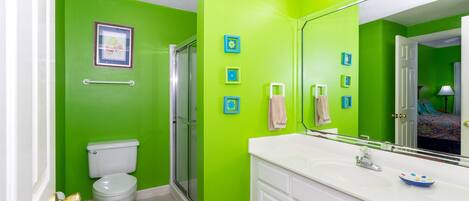 Une salle de bain avec des murs verts, des toilettes blanches, une douche en verre et un meuble-lavabo blanc avec un miroir.