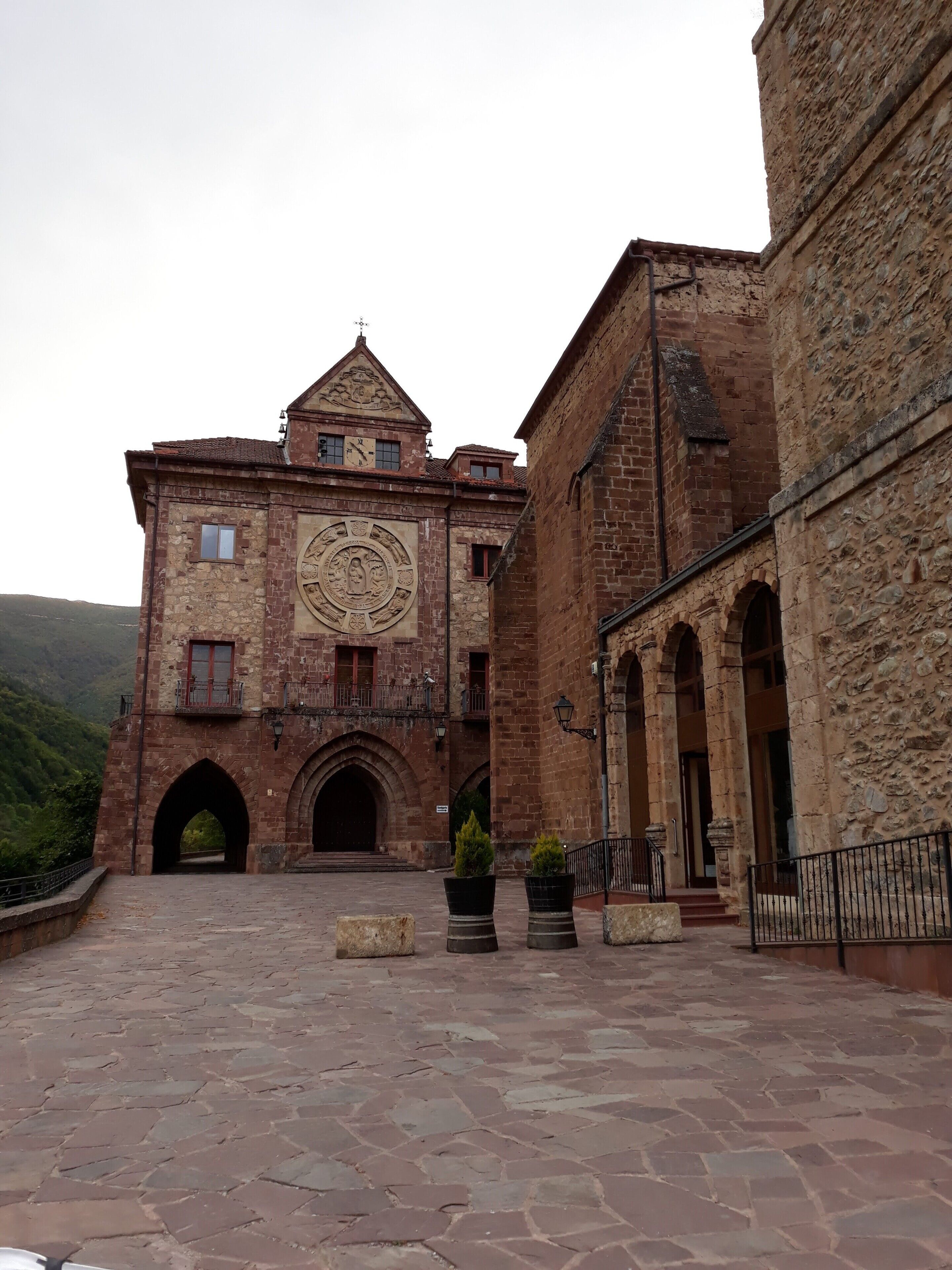 Un edificio histórico con un gran emblema circular en la fachada, arcos de entrada y un patio empedrado.