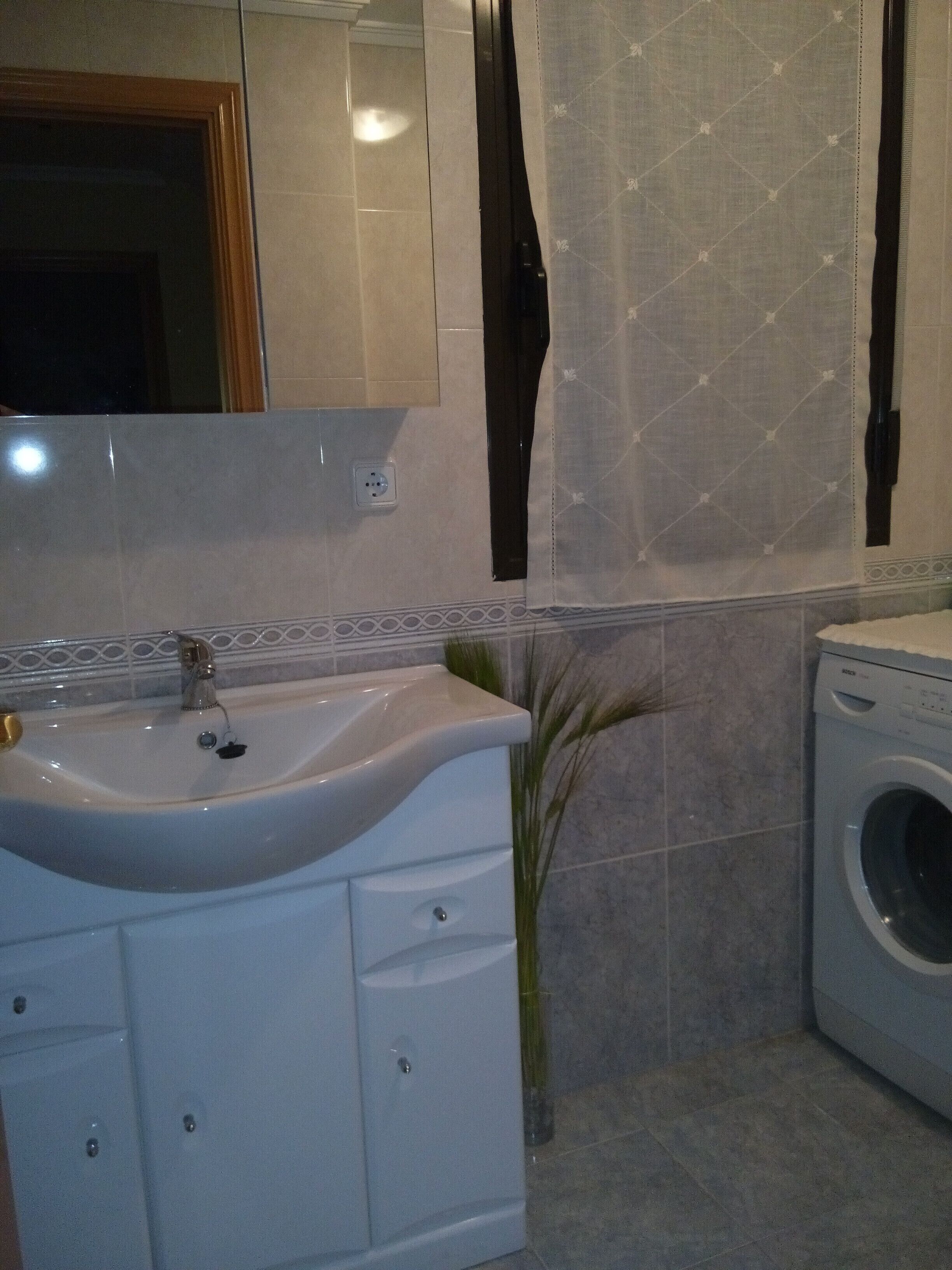 Een badkamer met een wastafel, spiegel en wasmachine.
