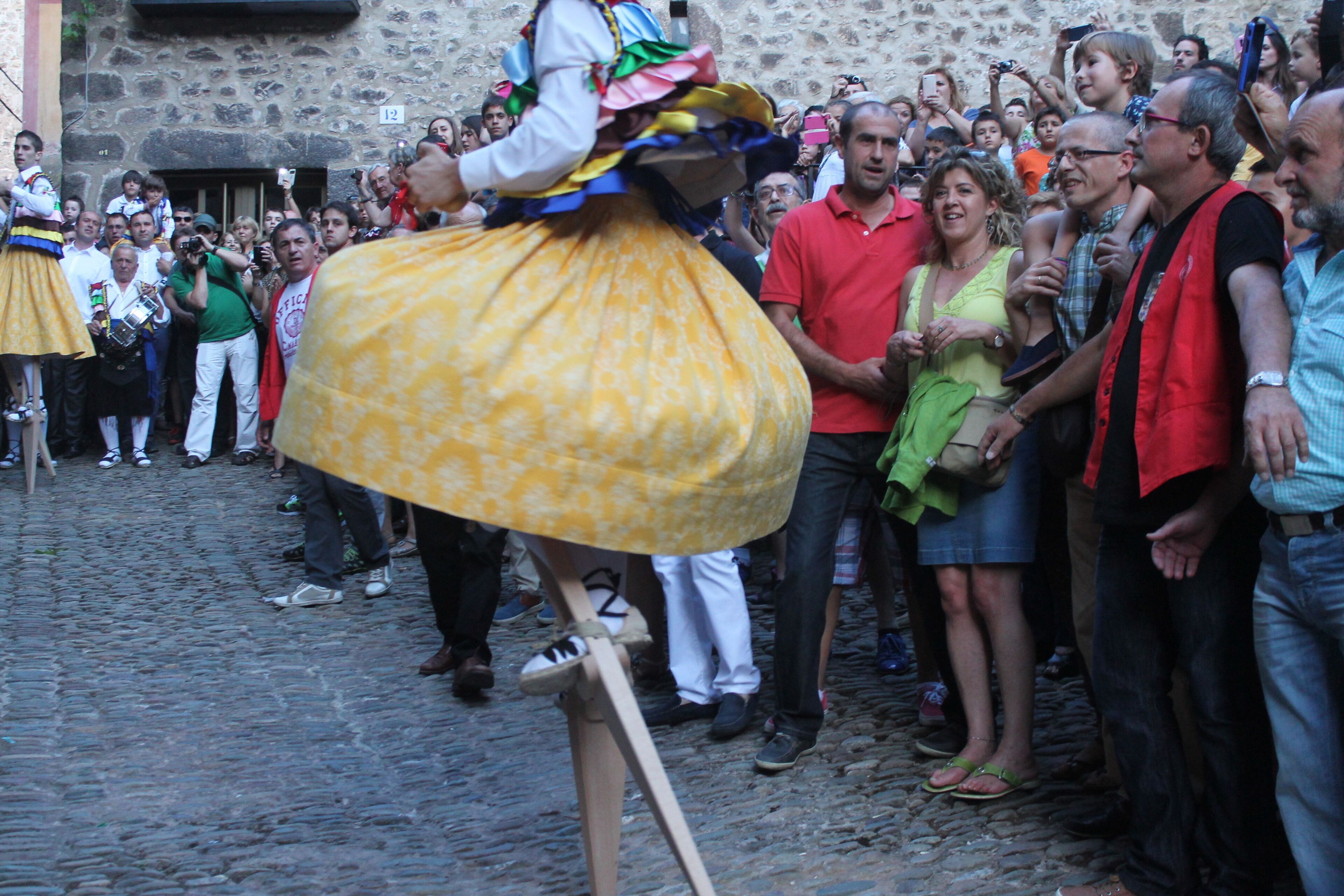 Una calle adoquinada con una multitud de personas observando a alguien con un vestido amarillo.