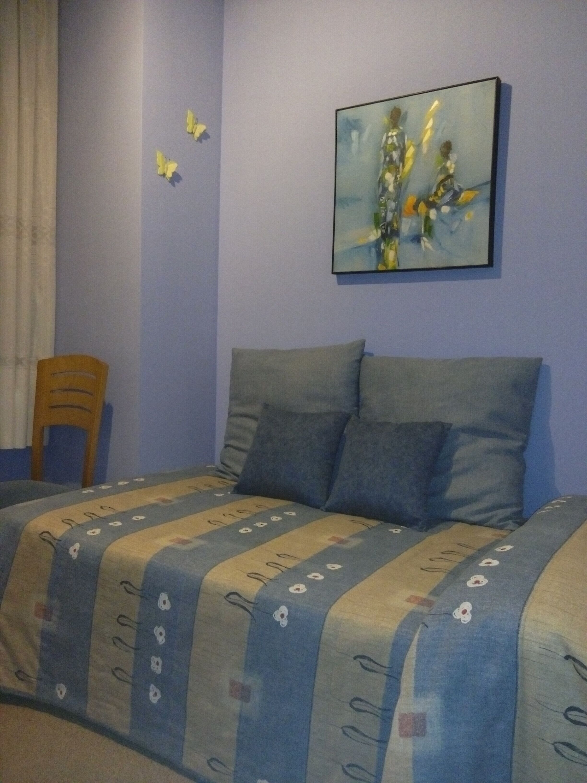 Un dormitorio con cama, almohadas, una silla y un cuadro en la pared.