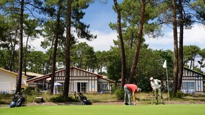 A golf course with a clubhouse, surrounded by tall pine trees.