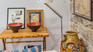 Una habitación con una mesa de madera, dos cuencos, una lámpara, un florero y una cama con almohadones estampados.