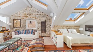 Un espacioso dormitorio en el ático con pared de piedra, un sofá blanco, cama y tragaluces.