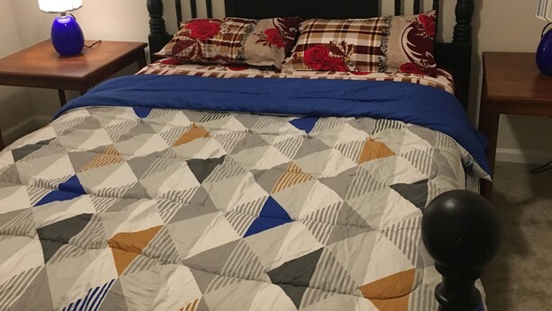 En seng med et geometrisk mønstret sengetæppe, en mørk træhovedgærde og to sengeborde med lamper.