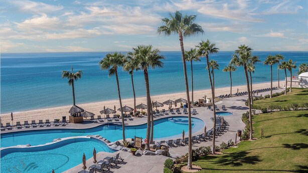 Ein Resort mit großem Pool, Palmen und Strand.