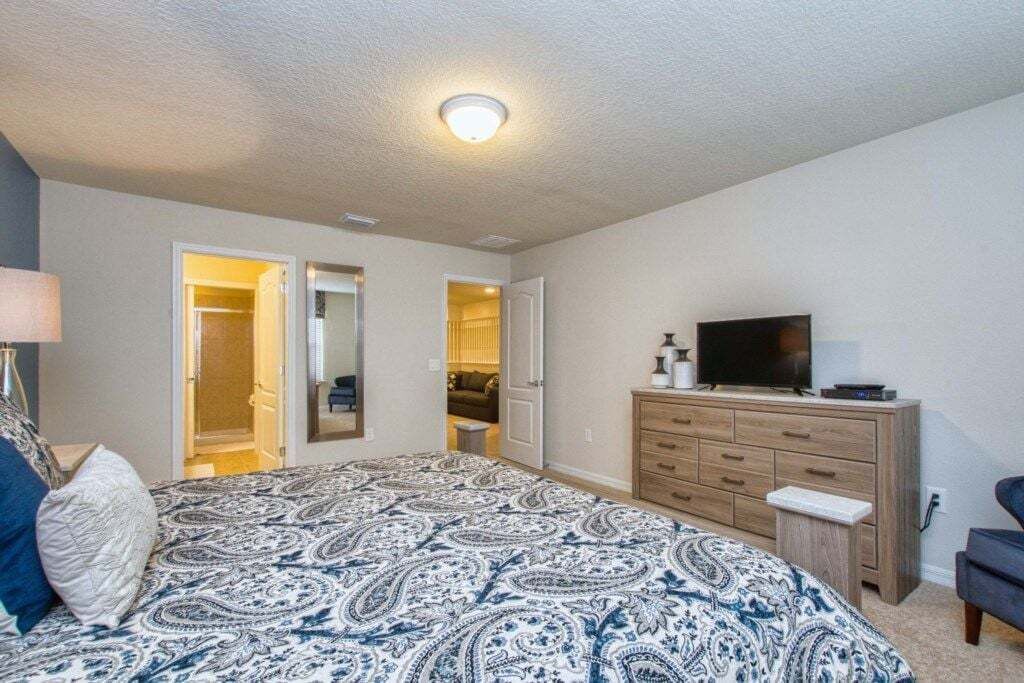Un dormitorio con cama, cómoda, televisor y armario con espejo.