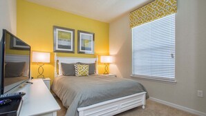 A bedroom with a bed, bedside tables, a TV, and a window with blinds. - 5BR Windsor Townhome | Private Splash Pool | Sleeps 12 | Dog Friendly | Near Disney (kissimmee)