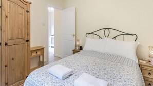 Une chambre à coucher comprenant un lit, une armoire en bois, une table de chevet et une porte donnant sur une autre pièce.
