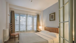 Ett hotellrum med en säng, en stol, ett nattduksbord, en lampa och ett fönster med gardiner.