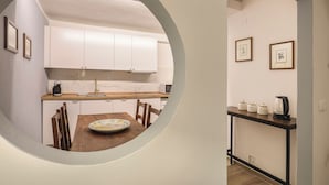 Ett modernt kök med vita skåp, ett matbord i trä och en kaffebryggare placerad på ett avlastningsbord.