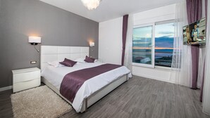 Une chambre moderne avec un grand lit, une table de chevet, un tapis moelleux, une lampe fixée au mur et une fenêtre donnant sur le coucher de soleil.