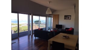 Relax in this stylish living space with a large sliding door leading to a sea view, a comfortable sofa, and a flat-screen TV.
