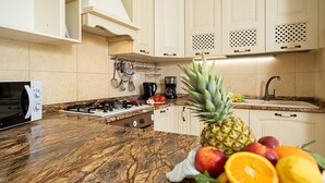 Une cuisine dotée d’un plan de travail en marbre, d’une cuisinière à gaz, d’une machine à café et d’un panier à fruits contenant différentes sortes de fruits.