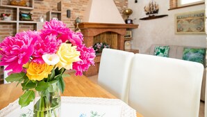 Un coin repas avec une table dressée pour deux personnes, un vase de fleurs, un mur en briques et une cheminée.