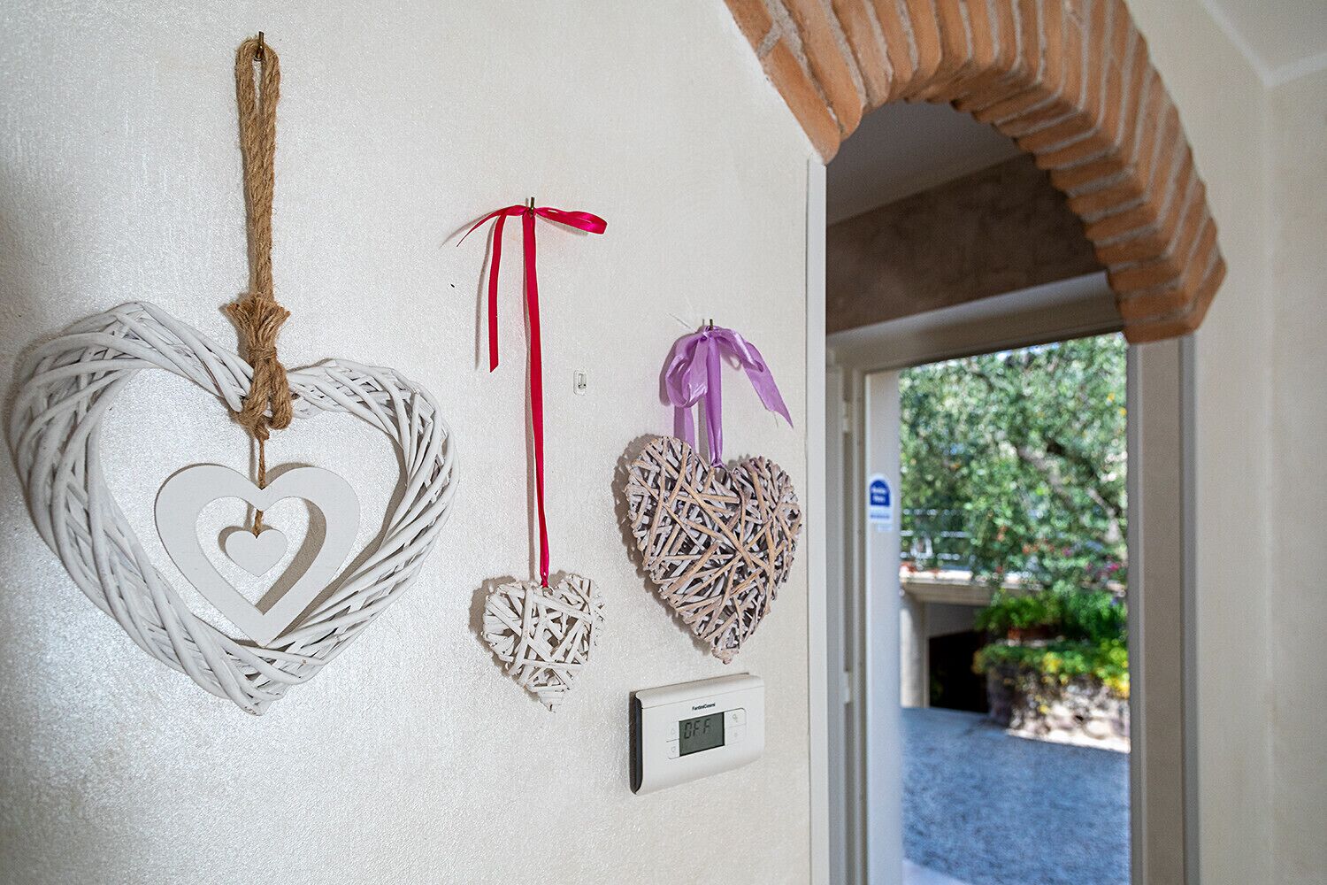 Three heart-shaped wall decorations, a thermostat, and a door leading to an outdoor area.
