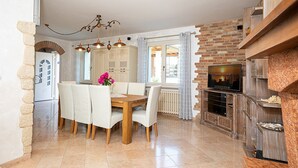 Un coin repas avec une table et des chaises en bois, un lustre et un mur de briques agrémenté d’une cheminée.