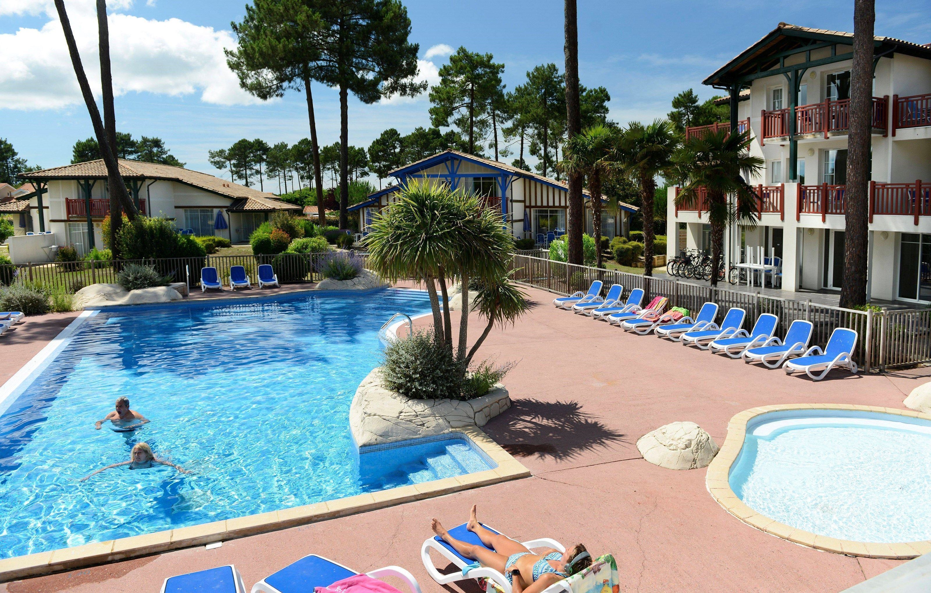 A pool area with lounge chairs, a small pool, and a building with balconies.