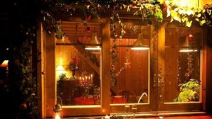 Ein gemütlich beleuchteter Raum mit Holzwänden, einem mit Grünpflanzen verzierten Fenster und einer Kerze auf der Fensterbank.