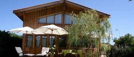 Una cabaña de madera con terraza, mobiliario exterior y un gran paraguas.