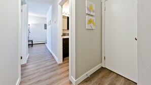 A hallway with wooden flooring, white walls, and a door at the end. There are two framed artworks on the wall. - Central, Modern and Cozy 1 Bedroom Retreat in the Heart of Tuxedo (Calgary)