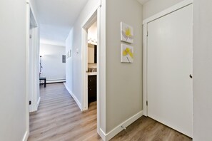 A hallway with wooden flooring, white walls, and a door at the end. There are two framed artworks on the wall. - Central, Modern and Cozy 1 Bedroom Retreat in the Heart of Tuxedo (Calgary)