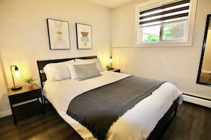 A neatly made bed with a dark headboard, two bedside tables with lamps, and two framed artworks on the wall.