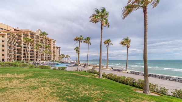 A beachfront hotel with multiple balconies, a pool area, and palm trees.