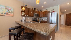 A kitchen with granite countertops, wooden cabinets, stainless steel appliances, and a bar area with stools.
