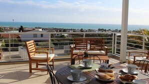 Eine Terrasse mit Holztischen und -stühlen und Blick auf das Meer, im Hintergrund eine Person, die geht.
