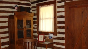 A cozy cabin room with a wooden cabinet, a chair, a small table with a basket, and a window with curtains.