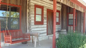 A log cabin with a porch, a swing, and a bench.