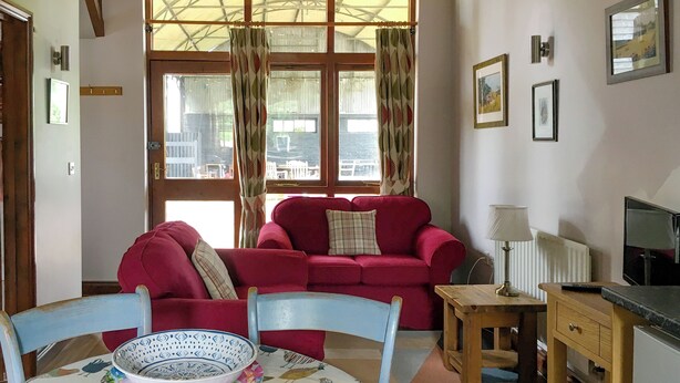 Una sala de estar con un sofá rojo, una mesa de comedor con mantel estampado de pájaros y un televisor sobre un soporte de madera.