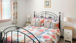 Un dormitorio con una cama, dos mesitas de noche, una lámpara de noche, una ventana con cortinas y un cuadro en la pared.