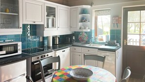 Una cocina con armarios blancos, microondas, estufa y pileta. Hay un mantel colorido sobre una mesa con un bol.