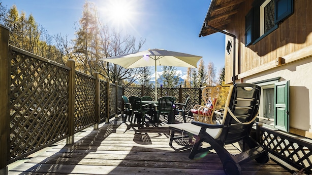 A wooden deck with a table and chairs, a large umbrella, and a wooden fence.