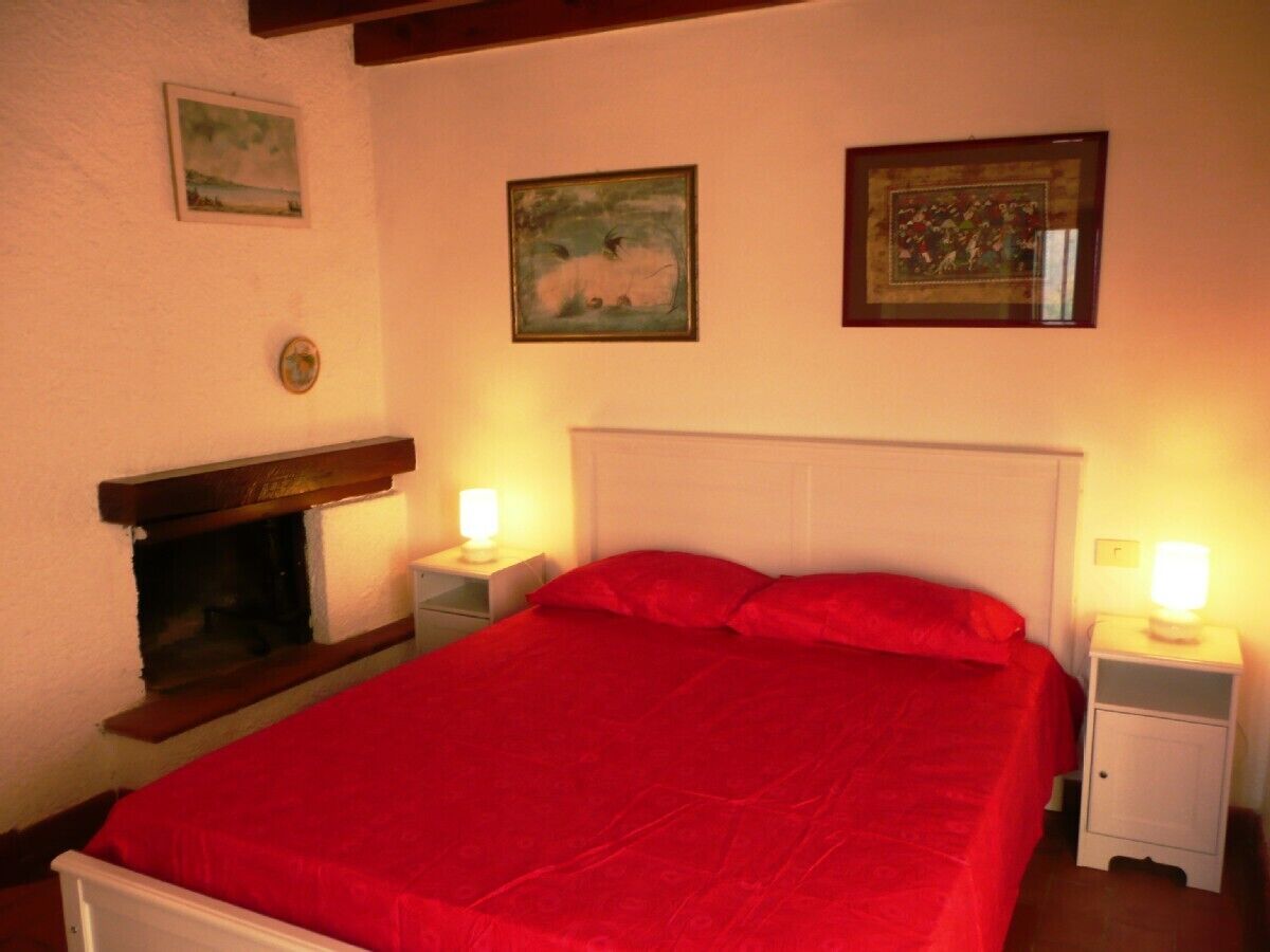 A bedroom with a large bed, two bedside tables, a nightstand, a fireplace, and three framed pictures on the wall.