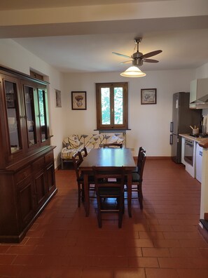 Un coin repas avec une table et des chaises en bois, un ventilateur de plafond et une fenêtre donnant sur les arbres.
