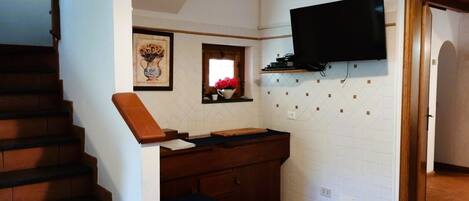 Una cocina con una escalera de madera, un televisor de pantalla plana montado en la pared y una ventana pequeña con un florero.