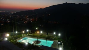 A nighttime view of a swimming pool with surrounding lights and a distant cityscape. - Villa with private swimming pool, garden & sea view Forte Dei Marmi   (Pietrasanta)