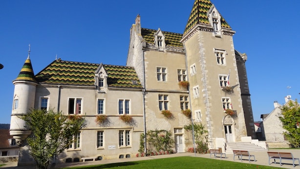 Un bâtiment historique doté d’une tour, de nombreuses fenêtres et d’une pelouse bien entretenue avec des bancs.