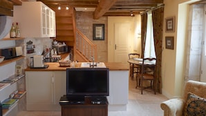 Une cuisine chaleureuse avec un îlot central en bois, un coin repas avec une table et des chaises, et un escalier menant à une autre pièce.