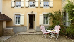 Un bâtiment à deux étages avec une façade jaune, des volets blancs et une petite entrée avec des marches.