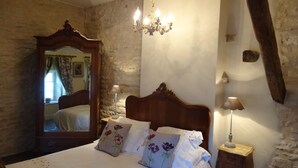 Une chambre à coucher avec un grand lit, une tête de lit en bois, un lustre, une table de chevet et un mur en pierre.