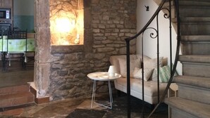 Un escalier en pierre, agrémenté d’une rampe en fer forgé, mène à un palier. Une table ronde sur laquelle est posée une lampe blanche se trouve sur ce palier.
