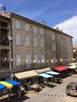 A stone building with multiple windows and balconies, a street market with colorful umbrellas, and a parked car.