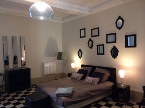 A bedroom with a checkered floor, a bed with multiple pillows, a dresser, a radiator, and several wall-mounted mirrors.